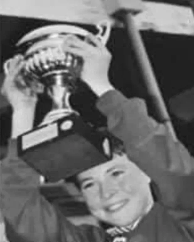 Liam as a boy, smiling and holding a trophy above his head.